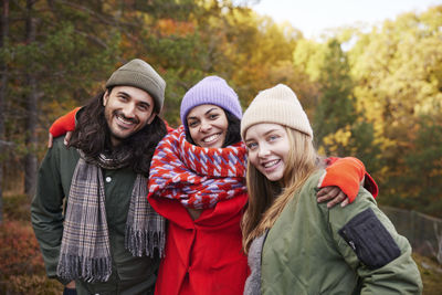 Portrait of smiling friends standing against trees