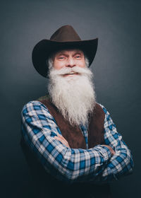 Portrait of happy senior man wearing cowboy hat against gray background