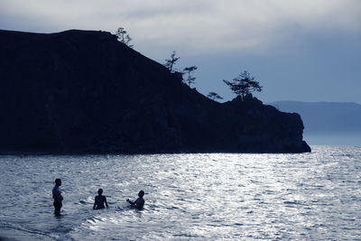 Silhouette people on mountain by sea against sky