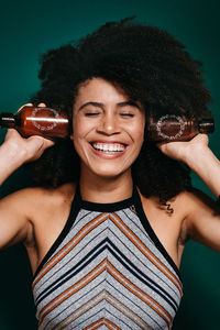 Smiling young woman holding bottles against colored background