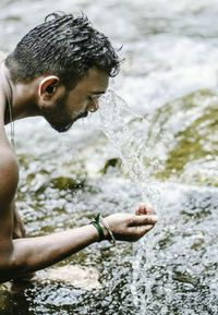 Shirtless man washing face from river water