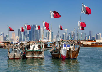 Sailboats moored on harbor against sky in city