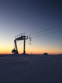 Silhouette of electricity pylon on snowy field against sky during sunset