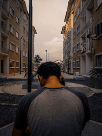 Rear view of man talking on phone while standing buildings