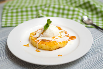 A ball of creamy vanilla ice cream on a slice of fried pineapple with caramel sauce. 