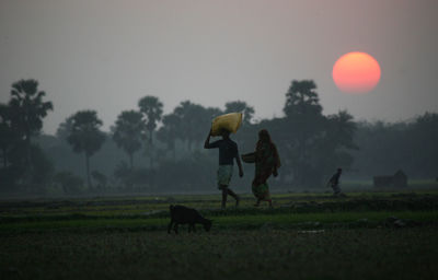 Farmers walking on field against sky