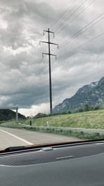 Road by electricity pylons against sky