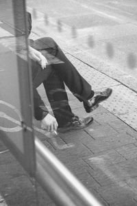 Man smoking while sitting at sidewalk seen through glass