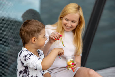 Happy blond woman and little boy sitting on terrace and eating sweets. mother and son enjoy