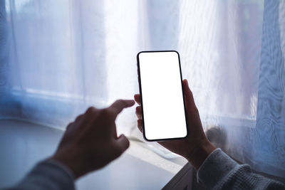 Mockup image of a woman holding mobile phone with blank white desktop screen