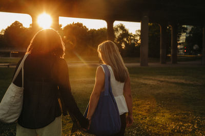 Teenage girls holding hands while walking at park during sunset