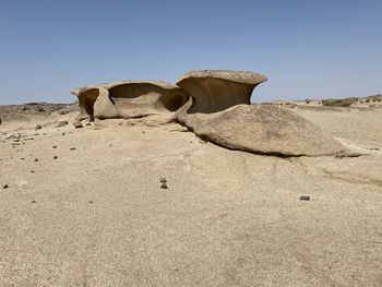 Rock on sand against clear sky