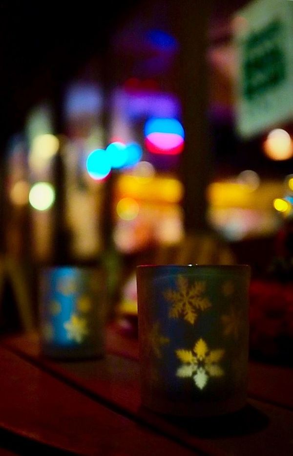 illuminated, night, indoors, focus on foreground, text, communication, lighting equipment, close-up, western script, selective focus, no people, light - natural phenomenon, multi colored, glass - material, table, defocused, glowing, reflection, still life, capital letter