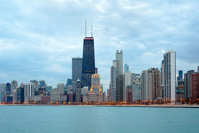 Modern buildings in city against cloudy sky by lake