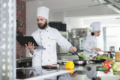 Chef looking at recipe in laptop while cooking meal in restaurant kitchen