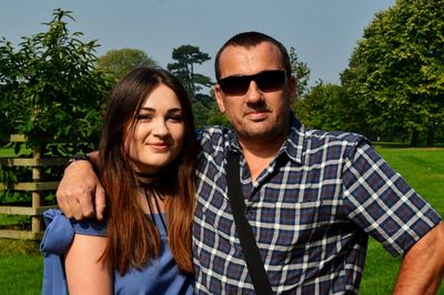 Portrait of couple standing at park on sunny day