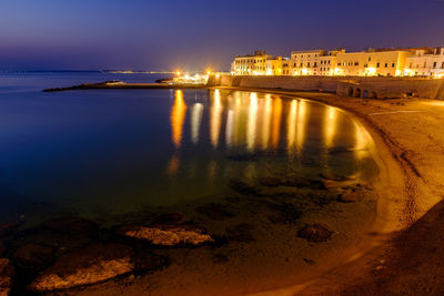 Illuminated city by sea against sky at night