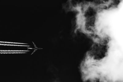 Low angle view of smoke emitting from airplane against sky at night