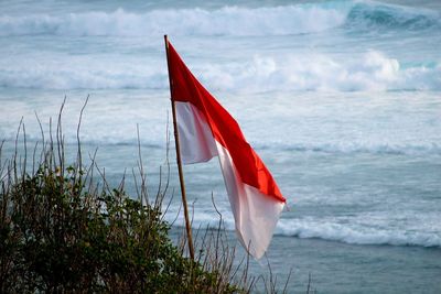 Red and white indonesian flag on sea against sky