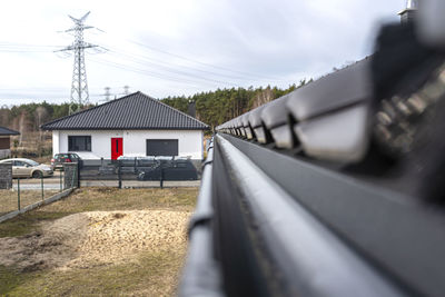 A metal, black gutter on a roof covered with ceramic tiles, visible house in the background.