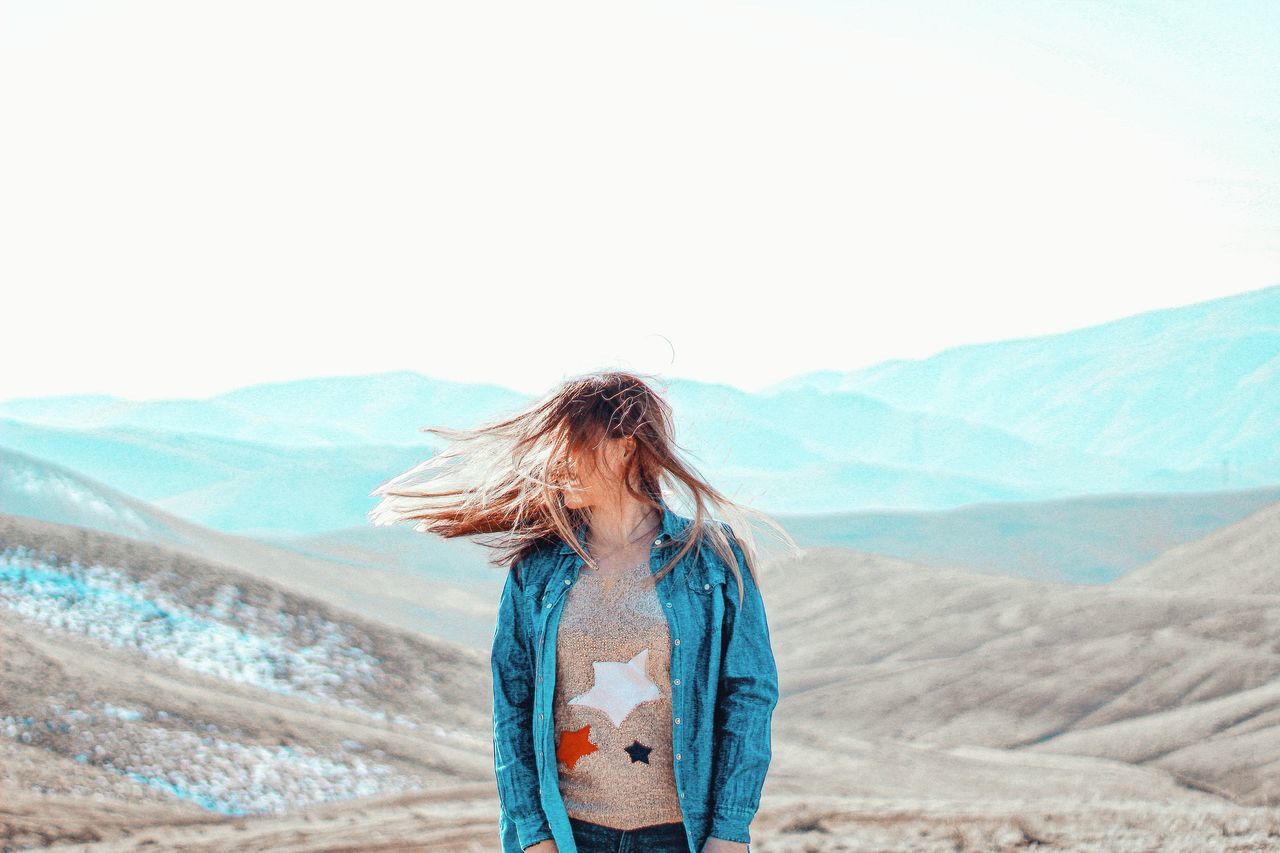 mountain, real people, leisure activity, one person, beauty in nature, sky, lifestyles, scenics - nature, environment, hairstyle, land, hair, long hair, standing, casual clothing, day, women, nature, copy space, mountain range, outdoors, wind
