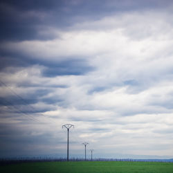 Electric pylons on field against sky