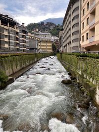 River flowing amidst buildings in city against sky