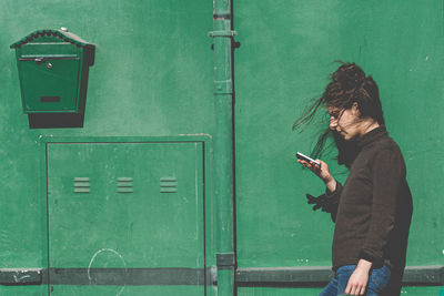 Young man using mobile phone while standing against green door