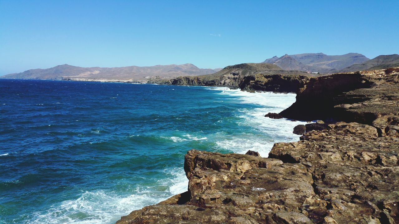 water, sea, mountain, clear sky, blue, scenics, tranquil scene, beauty in nature, tranquility, nature, rock - object, copy space, rock formation, idyllic, coastline, cliff, mountain range, beach, rock, shore