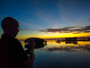 Man standing by lake against sky during sunset