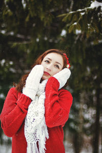 Redhead beautiful woman in red sweater and white gloves walking in the frozen winter forest.