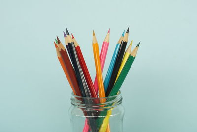 Close-up of multi colored pencils in jar against white background