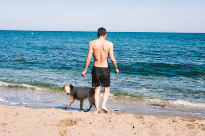 Full length of shirtless man with dog standing on beach