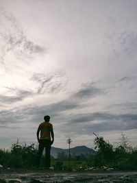 Rear view of man standing on field against sky