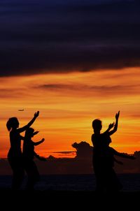 Silhouette people dancing against orange sky