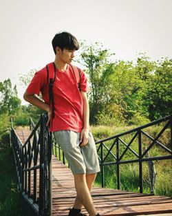Young woman looking away while standing by railing against trees