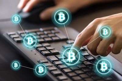 Digital composite image of cropped hands using computer keyboard by bitcoin icons