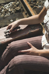 Midsection of woman holding suitcase while sitting on railroad track