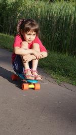 Cute girl sitting on skateboard in park