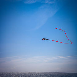 Low angle view of kite flying over sea against blue sky