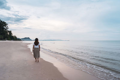 Rear view of woman on beach against sky