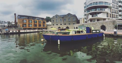 Boats moored on canal by buildings in city against sky