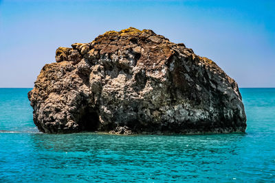 Rock formation in sea against clear blue sky