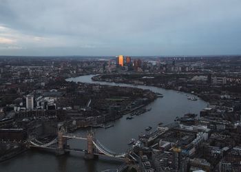 Tower bridge over thames river in city against cloudy sky