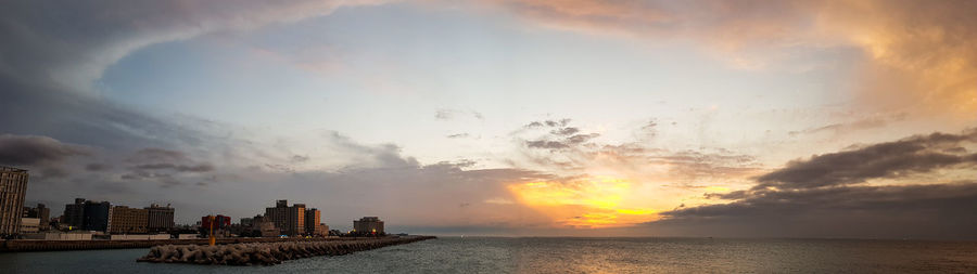 Sea by buildings against sky during sunset