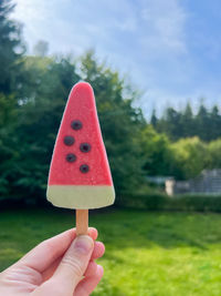 A woman holding an ice cream shaped like a watermelon outdoors in summer season