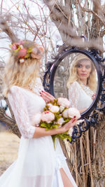 Young woman looking into mirror against bare tree