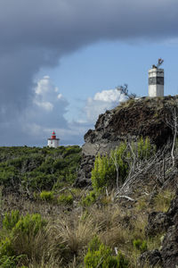 Lighthouse amidst rocks and buildings against sky