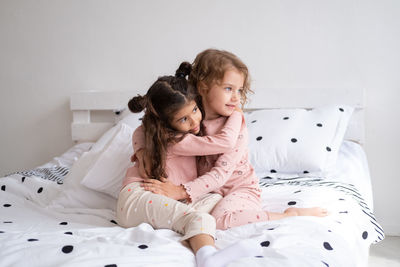 Cute sisters embracing while sitting on bed