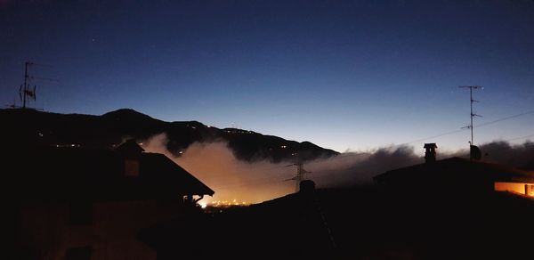 Silhouette houses and mountains against clear sky at sunset